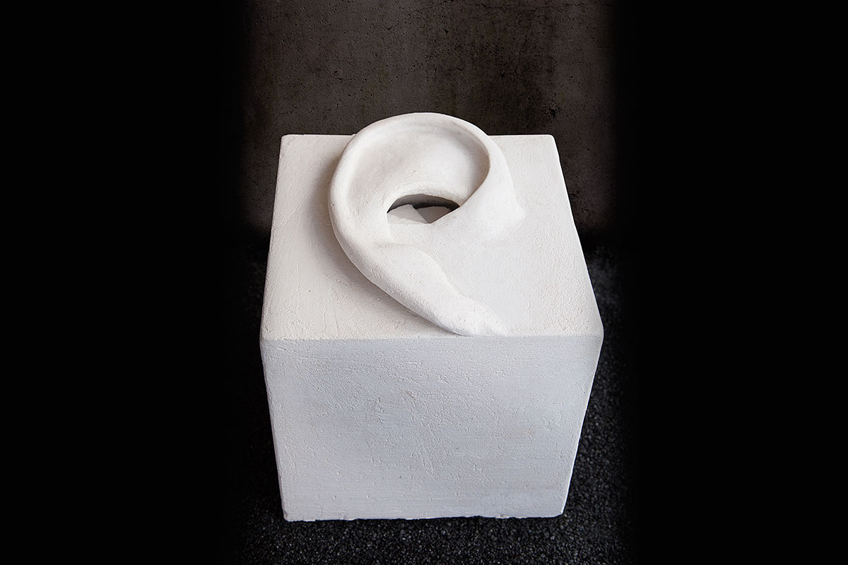 Cubo bianco in stucco con un grande orecchio in rilievo sulla sommità