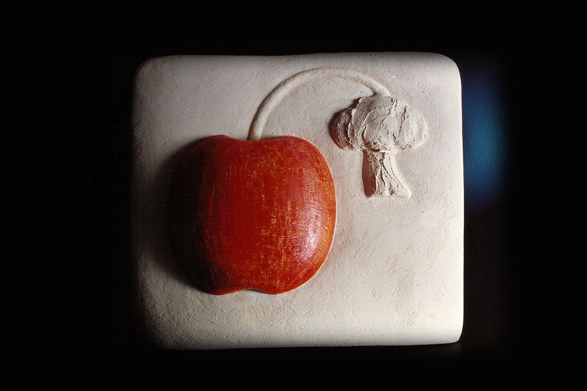 Rilievo in stucco bianco con una mela rossa e un piccolo albero